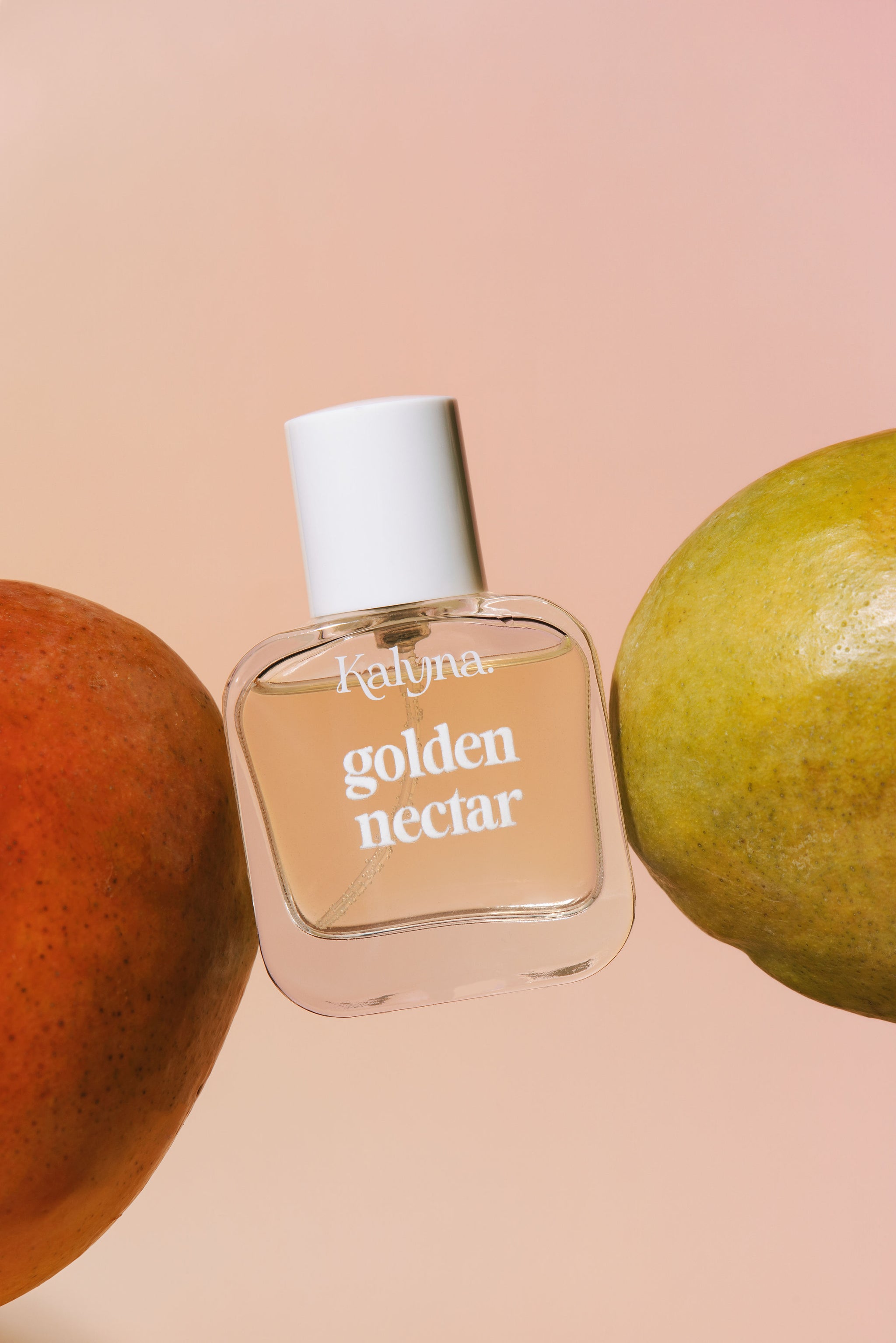 Perfume bottle labeled 'golden nectar' by Kalyna with mangoes on a peach background