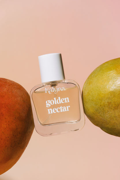 Perfume bottle labeled 'golden nectar' by Kalyna with mangoes on a peach background