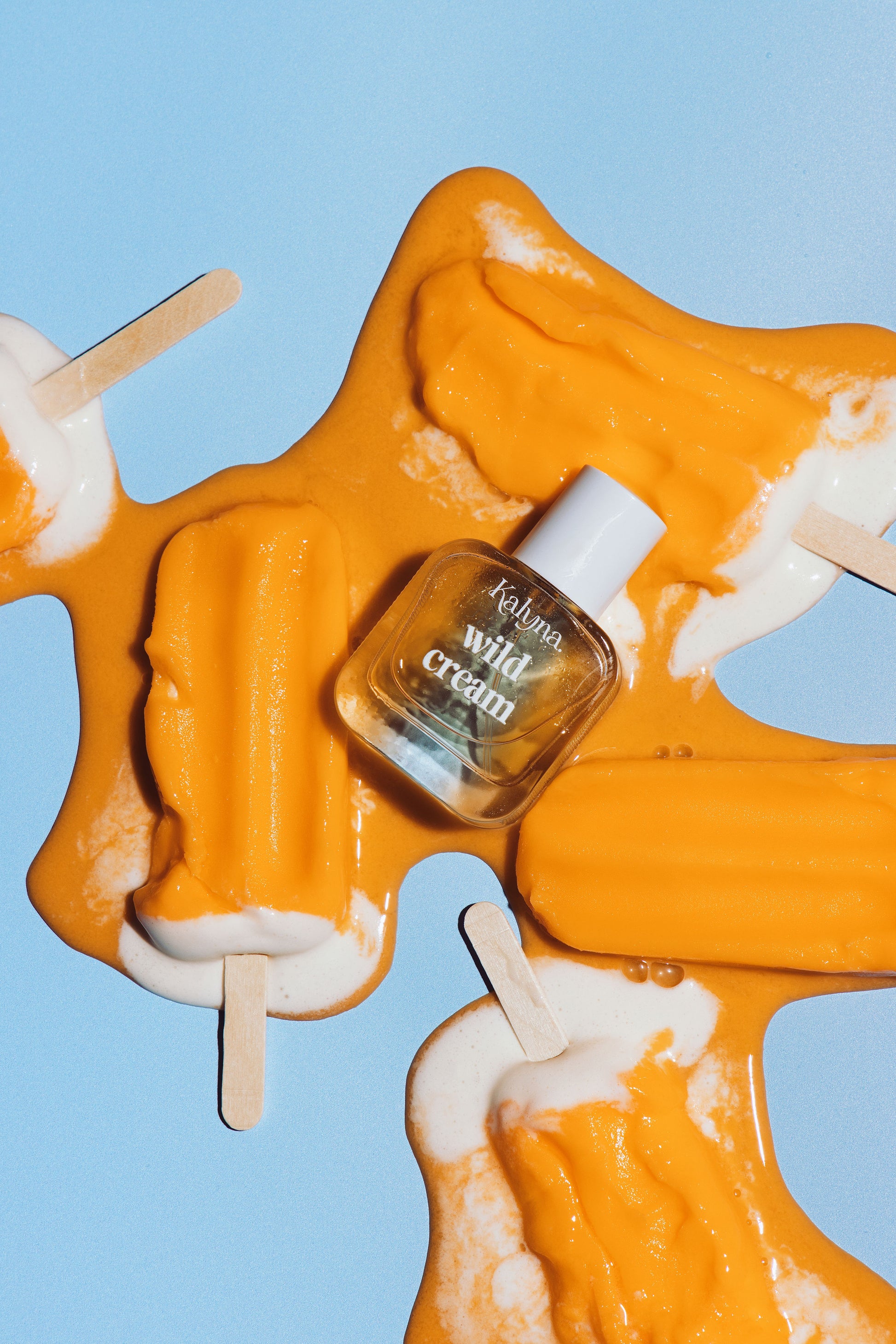 Small bottle labeled 'wild cream' on orange and white popsicles against a blue background