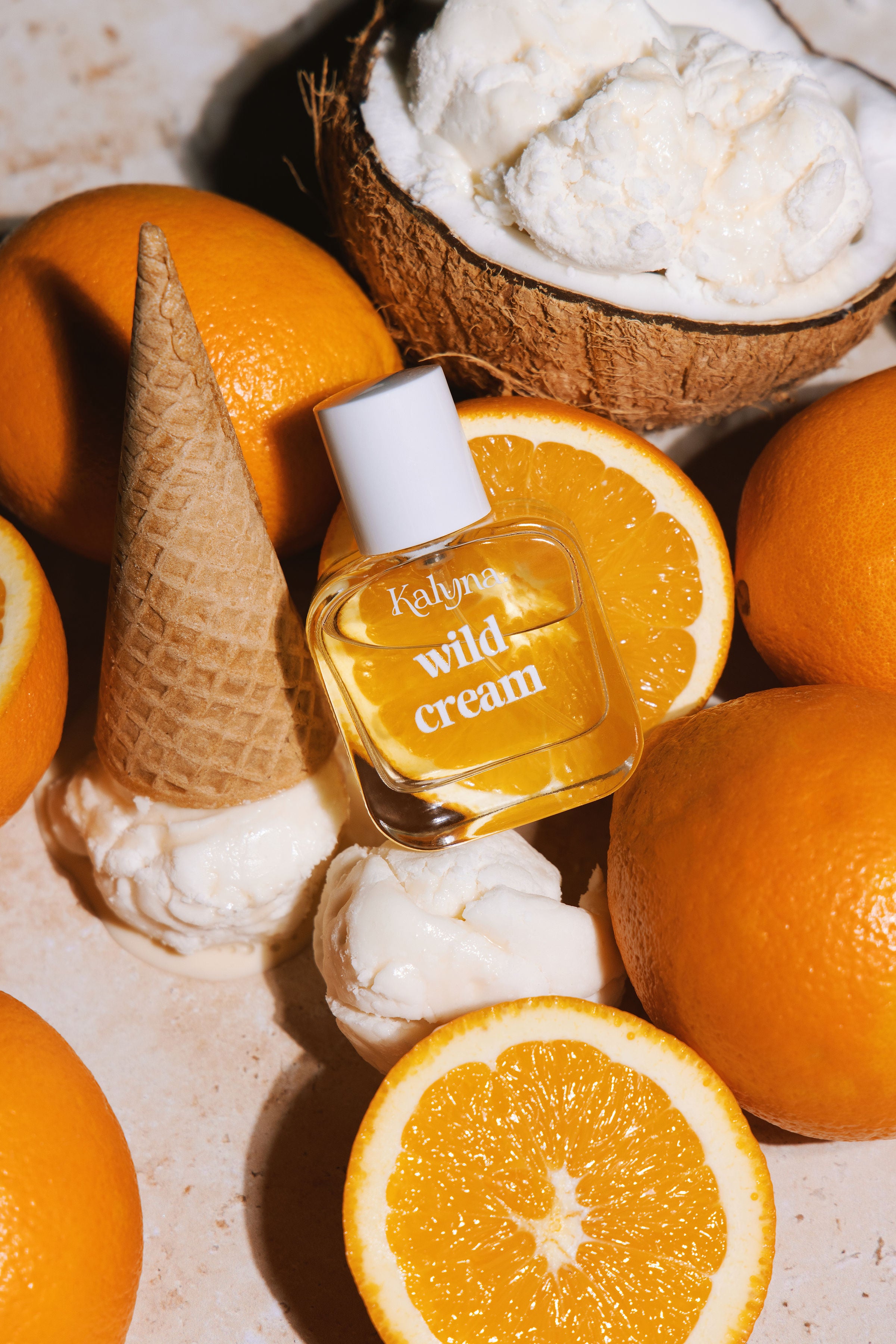 Small bottle labeled 'wild cream' surrounded by oranges and a coconut on a textured surface.