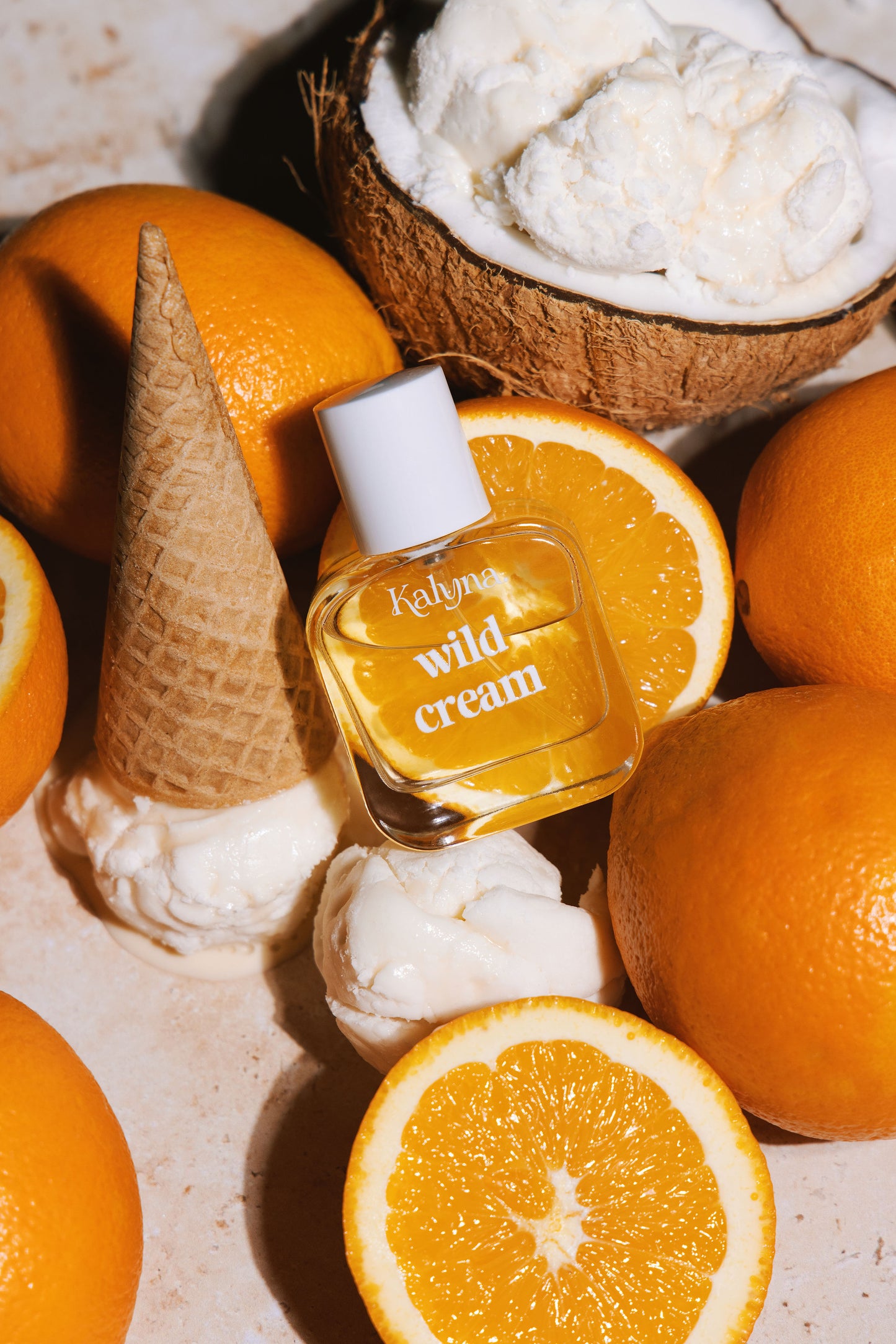 Small bottle labeled 'wild cream' surrounded by oranges and a coconut on a textured surface.